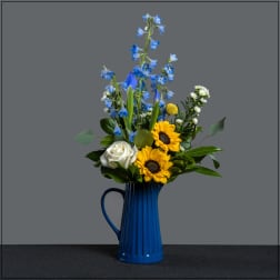 Blue delphiniums and sunflowers in a blue pitcher vase