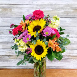 Mixed bouquet with sunflowers, pink and orange blooms in a glass vase