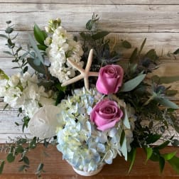 Pink roses and white flowers arranged with a starfish in a white vase