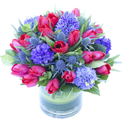 Bouquet of red tulips and purple flowers in a glass vase