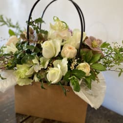 Mixed pale flowers arranged in a brown gift box with black handles