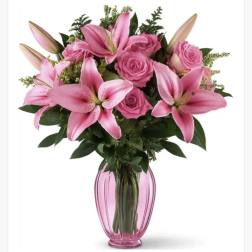 Pink lilies and roses arranged in a pink glass vase