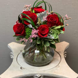 Red roses arranged in a glass vase with pink filler flowers