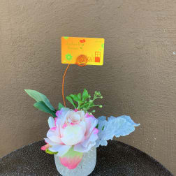 Small floral arrangement in a white textured pot with a gift card holder