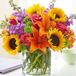 Bouquet of sunflowers, orange lilies, pink roses, and purple flowers in a glass vase