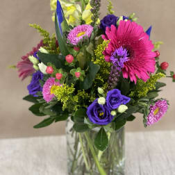 Bright mixed bouquet in a clear glass vase with pink, purple, and yellow blooms