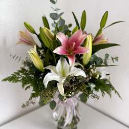 Pink and white lilies in a glass vase with greenery