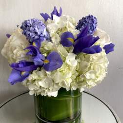 White hydrangeas and purple irises arranged in a green glass vase