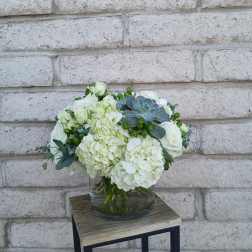 White floral arrangement in a glass vase with green accents