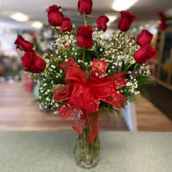 Red roses in a glass vase with baby's breath and a red bow