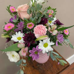 Mixed bouquet of pink, purple, and white flowers in a pink vase