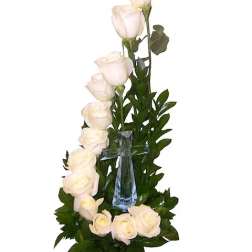 White roses arranged around a clear glass cross with greenery