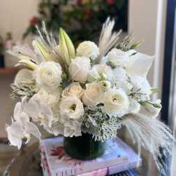 White floral arrangement in a dark green vase with orchids and roses