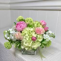 Pink peonies and roses arranged with green hydrangeas in a glass vase