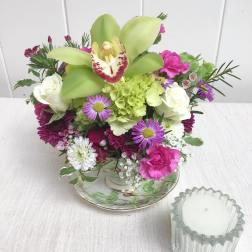 Mixed bouquet with green orchids, white roses, and pink flowers in a teacup-style vase