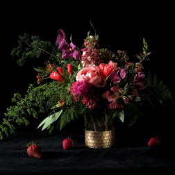 Mixed bouquet in a gold textured vase with strawberries on a dark surface