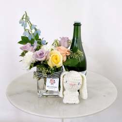 Mixed pastel roses in a glass vase with a plush bunny and bottle