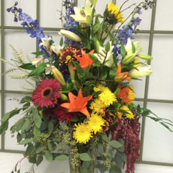 Tall mixed bouquet in a glass vase with lilies, gerbera daisies, and blue flowers