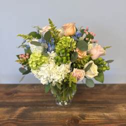 Mixed bouquet of white and green hydrangeas with peach roses and blue flowers in a glass vase