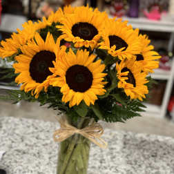 Bouquet of bright sunflowers in a clear glass vase with a raffia bow