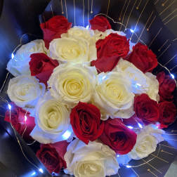 Bouquet of red and white roses wrapped in black paper with string lights