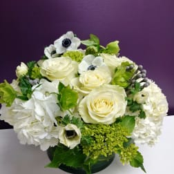 White roses and hydrangeas with green accents in a low vase arrangement