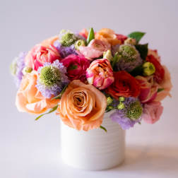 Mixed bouquet of peach, pink, and purple flowers in a white vase