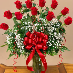 Red roses in a clear glass vase with baby's breath and a red bow