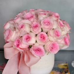 Pink and white roses arranged in a white vase with a pink ribbon