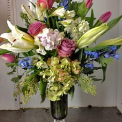Bouquet of pink roses, white lilies, and blue flowers in a glass vase