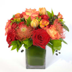 Red and orange floral arrangement in a square glass vase