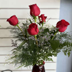 Red roses arranged in a burgundy vase with airy filler flowers