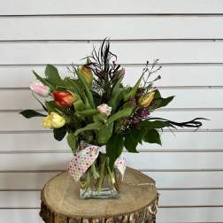 Mixed tulips and greenery in a clear glass vase with a polka-dot ribbon