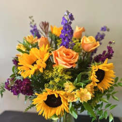 Bouquet of sunflowers, peach roses, and purple flowers in a glass vase