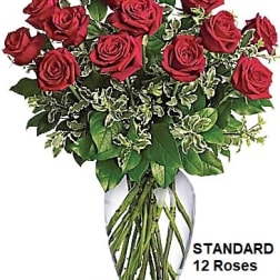 Arrangement of a dozen red roses with variegated foliage in a clear glass vase