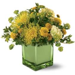 Yellow and white floral arrangement in a green glass vase