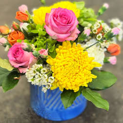 Bright mixed bouquet of pink roses, yellow mums, and small white blooms in a blue ceramic vase
