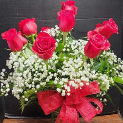 Red roses arranged in a glass vase with white baby's breath and a red ribbon