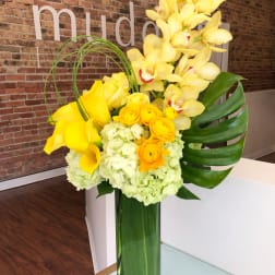 Yellow orchids, calla lilies, and roses arranged in a tall glass vase