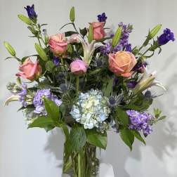 Mixed bouquet of pink roses, lilies, and purple flowers in a glass vase