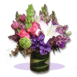 Mixed bouquet with white lily, purple hydrangea, and pink blooms in a glass vase
