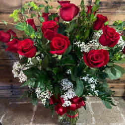Red roses in a glass vase with white filler flowers and a red ribbon