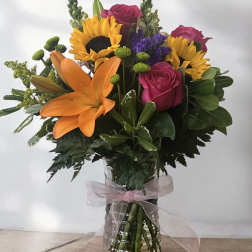 Mixed bouquet with sunflowers, roses, and an orange lily in a glass vase