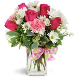 Pink roses and white daisies in a clear glass vase with a pink ribbon