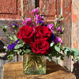 Red roses and purple flowers in a clear glass vase