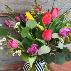 Colorful tulip bouquet in a glass jar with a striped ribbon