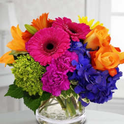 Colorful bouquet of gerbera daisies, roses, and hydrangeas in a glass vase
