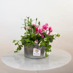 Oval metal planter with pink flowers, white blooms, and a small bird figurine.