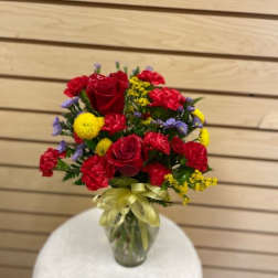 Bouquet of red roses, carnations, and yellow and purple filler flowers in a glass vase