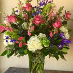 Tall mixed bouquet of pink roses, purple irises, and white hydrangeas in a glass vase